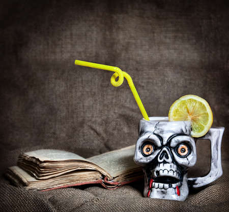 Skull mug with lemon and yellow stick near old book at textured background on Halloween partyの写真素材