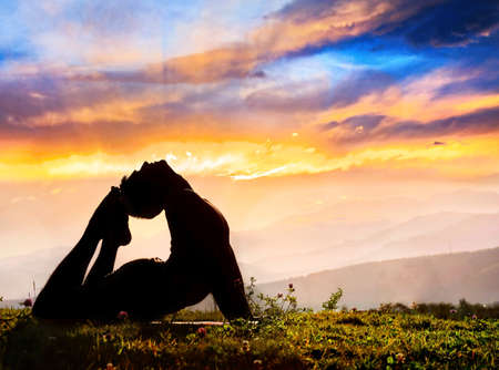 Yoga Raja Kapotasana backward bending pose by Man in silhouette on the grass outdoors at mountains...