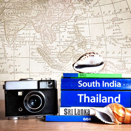 Retro photo camera near Guide books on the table with Seashell on its at old map background. Books with titles: South India, Bali, Sri Lanka, Goa, Thailandの写真素材