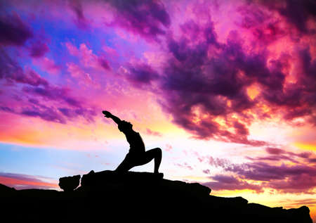 Yoga virabhadrasana I warrior pose by man silhouette with purple dramatic sunset sky background. Free space for text and can be used as template for web-siteの写真素材