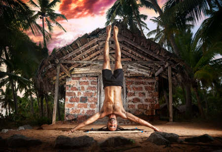 Yoga mukta hasta shirshasana, head stand pose by fit man with dreadlocks on the beach near the fishermen hut in Varkala, Kerala, Indiaの写真素材