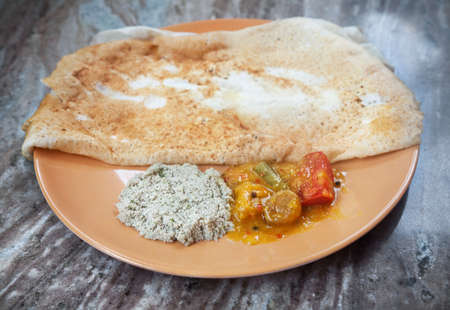 Indian traditional vegetarian masala dosa with potato inside, sambar and coconut chutney nearby at Indian restaurantの写真素材