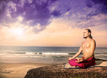 Yoga meditation in lotus pose by man with long hair in red trousers on the cliff near the ocean in Varkala, Kerala, Indiaの写真素材
