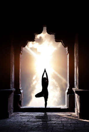 Yoga vrikshasana tree pose by man silhouette in old temple arch at dramatic sunset sky background. Free space for textの写真素材