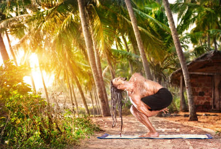 Yoga twisted pose by fit man with dreadlocks on the beach near the fishermen hut in Varkala, Kerala, Indiaの写真素材