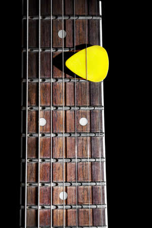 Yellow guitar pick on the fingerboard close up isolated on black backgroundの写真素材