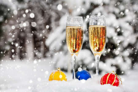 Two glasses with champagne and colorful Christmas balls on the snow in Christmas timeの写真素材