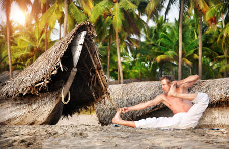 Yoga aakarna dhanurasana archer pose by fit man in white trousers on the beach near the fishermen boats in Indiaの写真素材