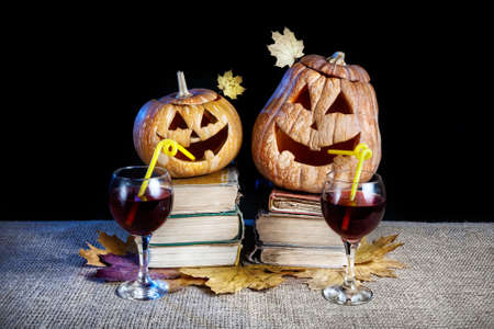 Funny Halloween pumpkins drinking wine on the heap of books at black backgroundの写真素材