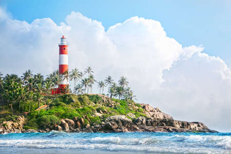 Lighthouse on the rocks near the ocean at blue sky with big white clouds in Kovalam, Kerala, India  の写真素材