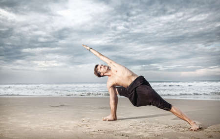 Yoga utthita parshvakonasana pose by man in black trousers on the beach near the ocean in Indiaの写真素材