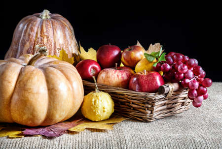 Pumpkins, apples in the basket, grapes and autumn leaves at black backgroundの写真素材