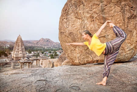 Woman doing yoga dancer pose near Virupaksha temple in Hampi, Karnataka, India