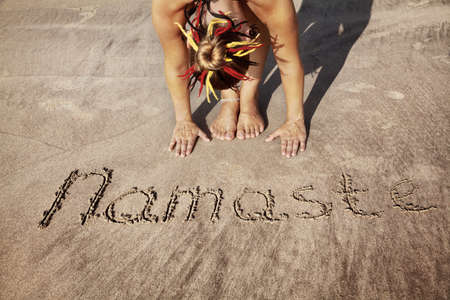 Woman doing yoga on the beach near Namaste handwriting in Goa, Indiaの写真素材