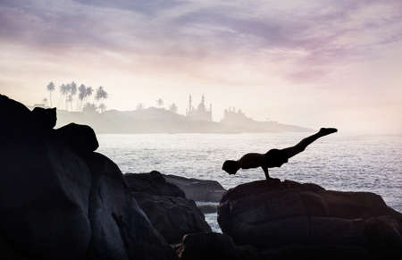 Man doing Yoga handstand on the rocks at ocean and mosque backgroundの写真素材