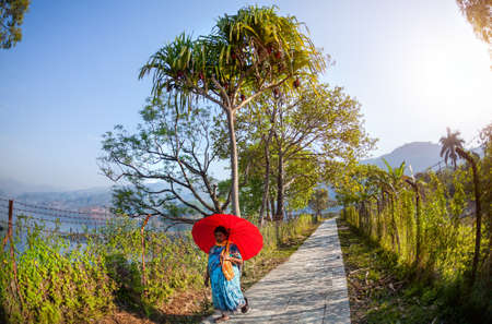 POKHARA, NEPAL - APRIL 21, 2014  Nepali woman with red umbrella walking down the road near Fewa Tal in the morningのeditorial素材