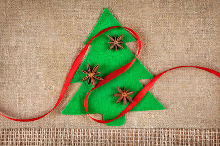 Christmas tree from felt with star anise and red ribbon on brown sackclothの写真素材