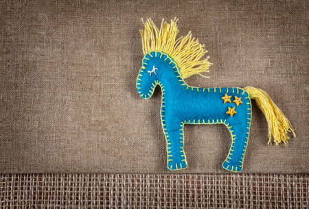 Blue horse toy from felt with yellow star buttons on brown sackcloth backgroundの写真素材