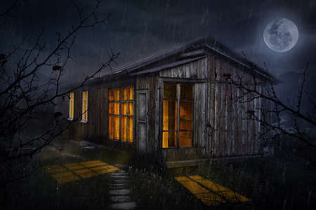 Rural house with glowing windows at night sky with moonの写真素材