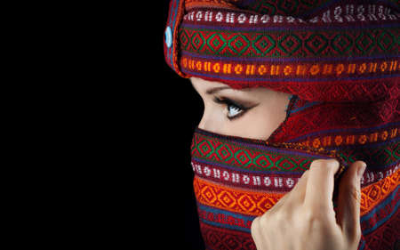 Oriental woman in turban covering her face on black backgroundの写真素材