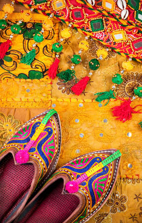 Colorful ethnic shoes and gipsy belt on yellow Rajasthan cushion cover on flea market in Indiaの写真素材