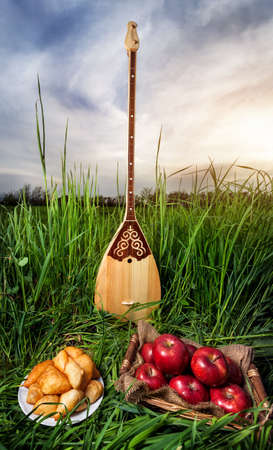 Dombra Kazakh instrument, apples and baursak dish on the grass at sunset skyの写真素材
