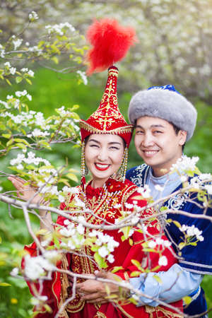 Happy couple in Kazakh costumes in Spring Blooming apple garden of Almaty, Kazakhstan, Central Asiaの写真素材