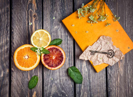 Oranges, lemon, yellow notebook, key and white flowers at wooden backgroundの写真素材