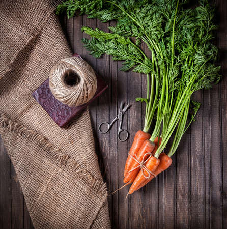 Raw carrot with green leaves near scissors and rope on sackcloth and wooden backgroundの写真素材