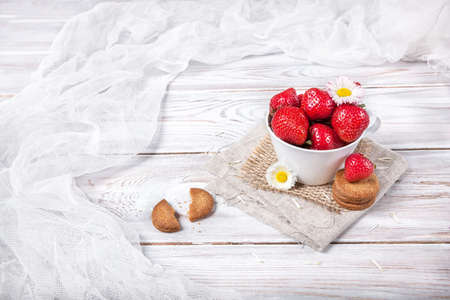 Strawberry in the cup with white flower and cookies on wooden tableの写真素材