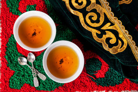 Kazakh national hat and black tea in two teabowls on the ethnic red carpet with oriental green patternの写真素材