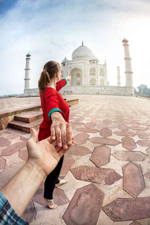 Woman in red Indian costume holding man by hand and pointing to Taj Mahal in Agra, Uttar Pradesh, Indiaの写真素材
