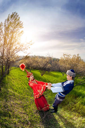 Kazakh woman in red dress dancing with man in Spring apple garden in Almaty, Kazakhstan, Central Asiaの写真素材