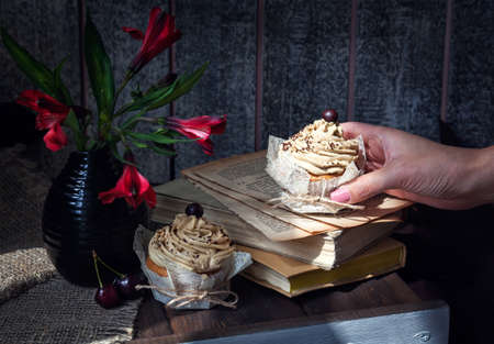 Woman hand holding chocolate homemade cupcake on the books near flowersの写真素材