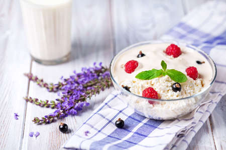 Cottage cheese with cream and berries on the table with violet flowers and glass of milkの写真素材