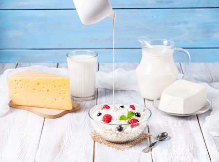Cottage cheese with cream and berries near other dairy products at blue wooden background