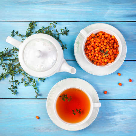 Herbal and berry tea in the cup near teapot and thyme leaves on blue wooden backgroundの写真素材