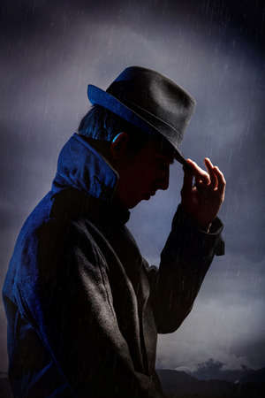 Man in black hat in the rain at dark overcast skyの写真素材