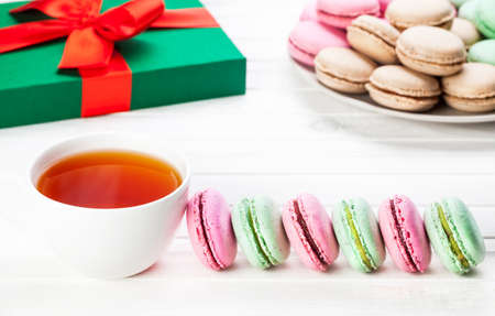 Colorful French macarons near cup of tea and present Christmas box on white backgroundの写真素材