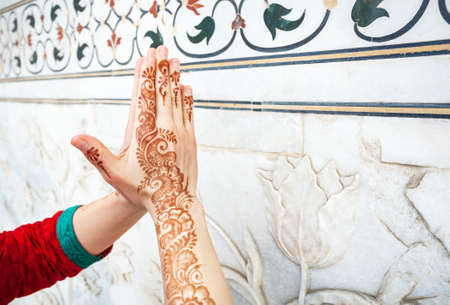 Woman in red Indian costume ding Namaste gesture by hand in henna paintings  near the marble wall with floral pattern in Taj Mahal in Agra, Uttar Pradesh, Indiaの写真素材