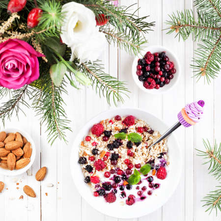 Decorative spoon with violet cupcake in the bowl with oats, berries and almond near winter flower...