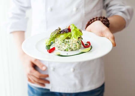 Chef holding Healthy Raw vegan salad in the white plate in restaurant