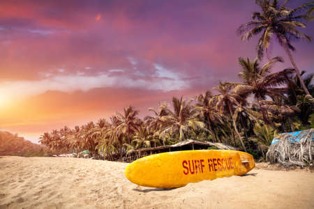 Yellow surf board at paradise tropical beach with purple cloudy sunset in Goa, India