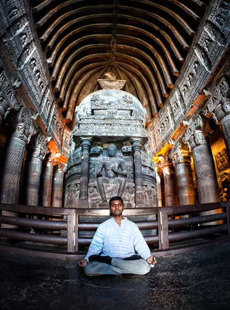 Indian Man doing meditation in lotus pose near the statue in ancient Ajanta cave near Aurangabad, Maharashtra, Indiaのeditorial素材