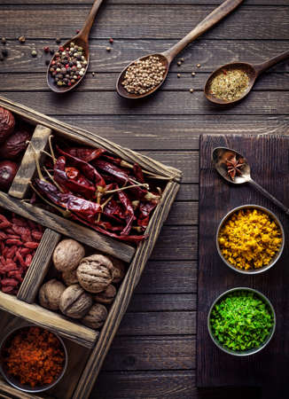 Spices, dry fruits and walnuts in the wooden box at wooden background with spoons nearbyの写真素材