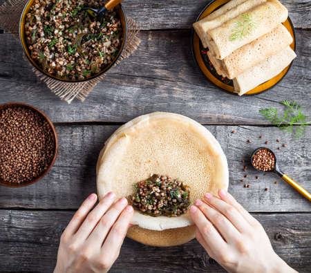 Woman rolling Russian vegan pancakes with buckwheat and Laminaria served in rustic style on Shrovetide holidaysの写真素材