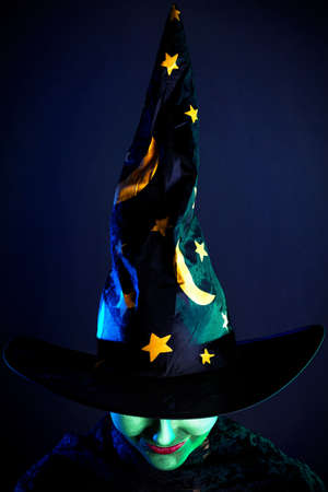 Witch with green skin in magic hat at Halloween on the dark backgroundの写真素材