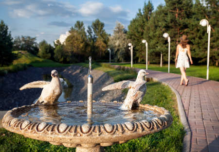 Fountain with dove statue and woman in white dress walking in the summer park in Almaty, Kazakhstanの写真素材
