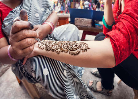 Indian woman making henna painting on tourist hand at main bazaar street in Delhiの写真素材