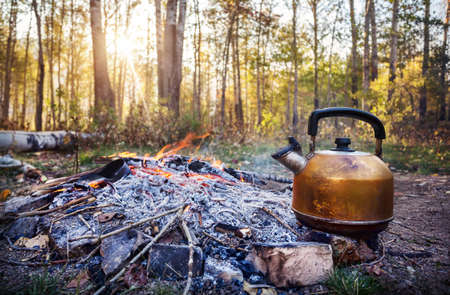Smoky tourist kettle on fire in morning forest at sunriseの写真素材